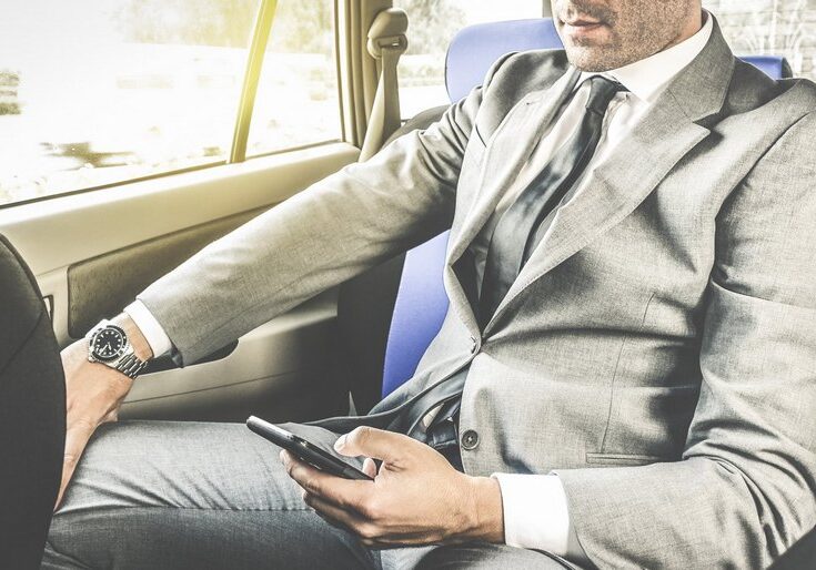 Young handsome businessman sitting in taxi cab while texting sms with smartphone - Business concept with modern man using smart phone - Soft vintage editing with artificial sunlight from window
